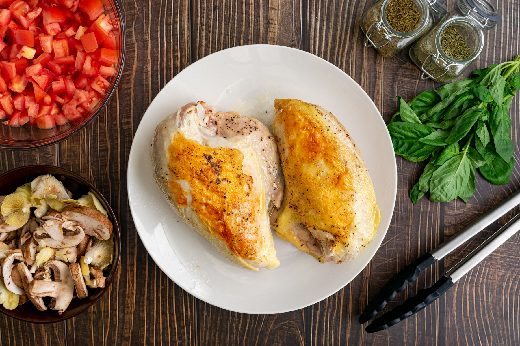 Browned Bone-in Skin-on Chicken Breasts on a White Plate: Seared chicken breasts surrounded by basil, wild mushrooms, and other ingredients